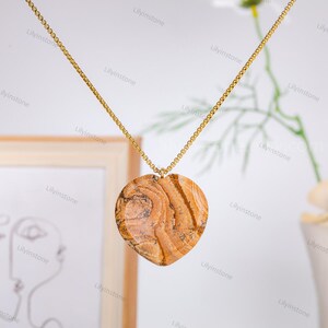 May include: A gold chain necklace with a heart-shaped pendant made of brown and beige patterned stone.