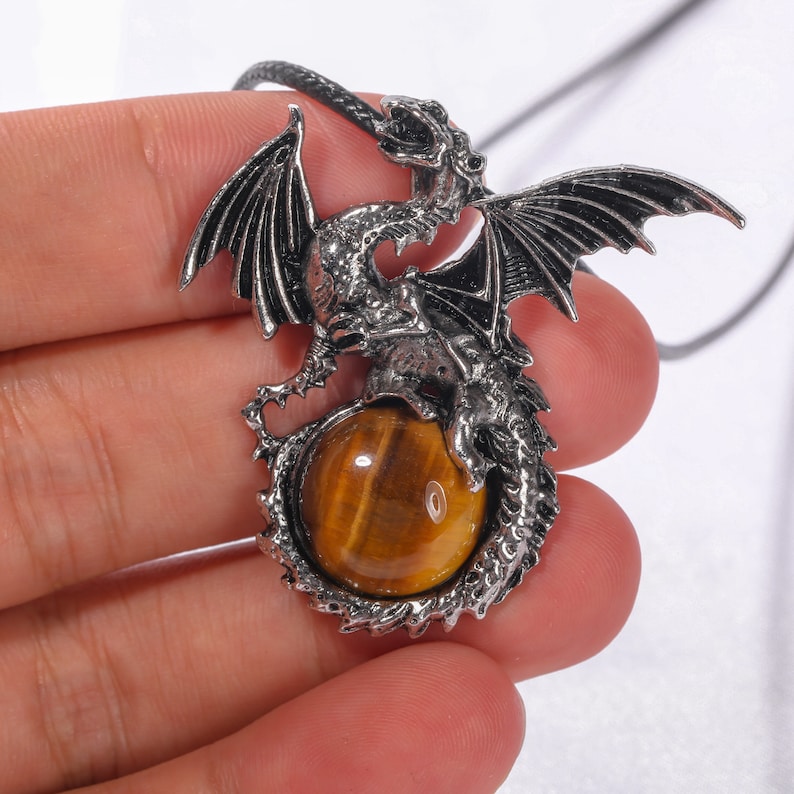 May include: Silver dragon pendant with a tiger's eye gemstone. The dragon is curled around the stone, with its wings spread out.