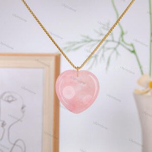 May include: A gold chain necklace with a pink heart-shaped pendant made of rose quartz.