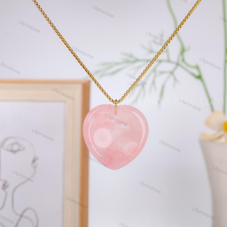 May include: A gold chain necklace with a pink heart-shaped pendant made of rose quartz.