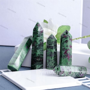 May include: Five green and pink gemstone points, also known as green and pink zoisite, are arranged on a white surface. The points are polished and have a natural, irregular shape.