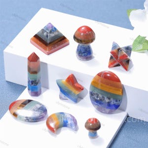 Peut inclure: Un ensemble de sept pierres de guérison des chakras en cristal de sept chakras dans différentes formes, notamment une pyramide, une étoile, un champignon, une lune croissante et un cercle. Les pierres sont faites de pierres précieuses superposées en rouge, orange, jaune, vert, bleu, indigo et violet.