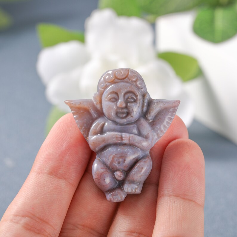 May include: A carved cherub figurine made of purple and brown agate. The cherub is sitting with its wings spread out and has a sweet expression on its face.