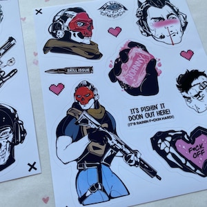 Puede incluir: Una hoja de pegatinas con varias ilustraciones, incluyendo un personaje con una m&aacute;scara de calavera roja, una mano sosteniendo una pastilla de jab&oacute;n con la etiqueta Johnny, una bala con la etiqueta Skill Issue y el texto It's pishin' it doon out here! (It's rainin f*ckin hard!).