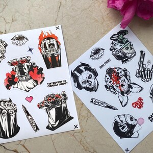 Puede incluir: Dos hojas de pegatinas blancas con ilustraciones gr&aacute;ficas en negro, blanco y rojo de equipo t&aacute;ctico, calaveras y personajes militares. El texto incluye "INTROVERT IN COMBAT MODE", "STAY FROSTY", "GHOST", "CHEER UP" y "MASK STAYS ON".