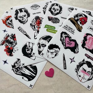 Puede incluir: Una colecci&oacute;n de hojas de pegatinas con diversas ilustraciones gr&aacute;ficas, incluyendo personajes con m&aacute;scaras de calavera, motivos militares y elementos de texto como "STAY FROSTY", "GHOST", "GET US A TEA", "F*CK OFF", "JOHNNY" y "ARE YOU UGLY?" en negro, blanco y rojo.