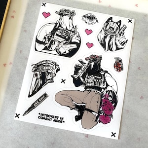 Puede incluir: Una hoja de pegatinas con ilustraciones t&aacute;cticas en blanco y negro, que incluyen figuras con equipo de combate, un casco, una granada, una bala con la etiqueta ONE SHOT y el texto INTROVERT IN COMBAT MODE, con peque&ntilde;os corazones rosas pixelados.
