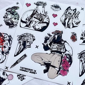 Puede incluir: Una hoja de pegatinas con ilustraciones en blanco y negro de equipo t&aacute;ctico, calaveras y figuras con ropa de combate. Los dise&ntilde;os incluyen textos como "STAY FROSTY", "ONE SHOT" e "INTROVERT IN COMBAT MODE", junto a peque&ntilde;os corazones pixelados.