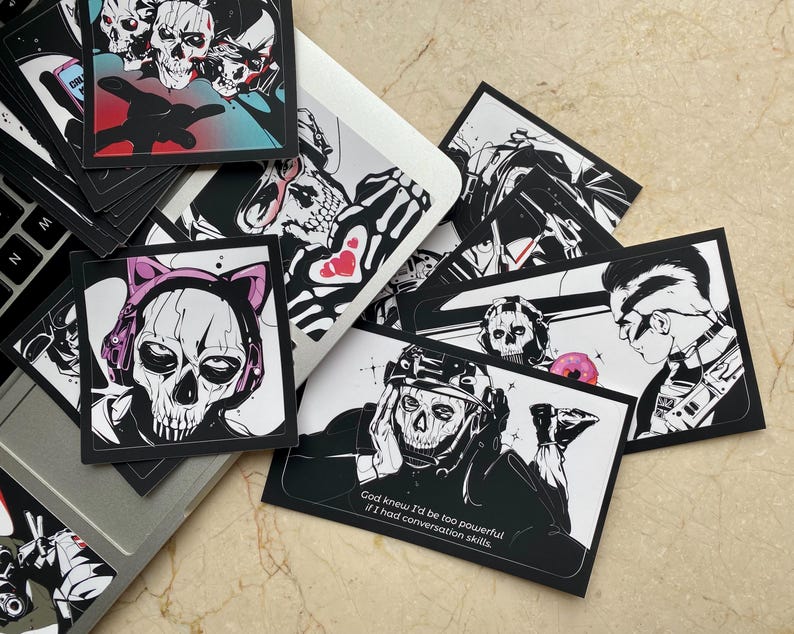 K&ouml;nnte beinhalten: Eine Sammlung von quadratischen und rechteckigen Aufklebern mit schwarz-wei&szlig;en Illustrationen von Charakteren mit Totenkopfmasken. Ein Aufkleber zeigt eine Figur mit rosa Katzenohren, ein anderer enth&auml;lt den Text, God knew I'd be too powerful if I had conversation skills.
