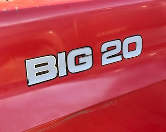 May include: Close-up of a red surface with the words "BIG 20" in white, outlined in black. The numbers and letters are large and bold, with a slight shadow effect. The surface has some scratches.