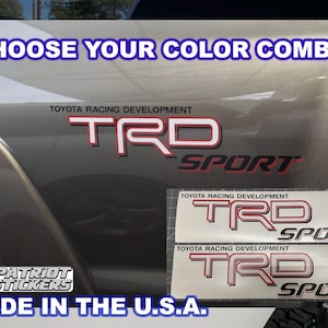 May include: Two Toyota Racing Development TRD Sport decals featuring red and white lettering with black outlines. The text CHOOSE YOUR COLOR COMBO! appears at the top, and MADE IN THE U.S.A. with a flag icon is at the bottom left corner.