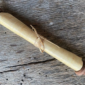 May include: A rolled up scroll tied with twine, with wooden ends. The scroll is on a rustic wooden surface.