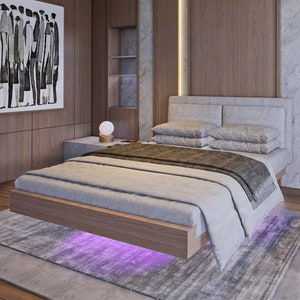 May include: A modern bedroom with a large bed, a bedside table, two chairs, and a small table. The walls are wood paneling and the bed has a white headboard and a gray comforter.