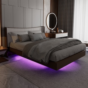 Op de afbeelding: Een moderne slaapkamer met een zwevend bed, een nachtkastje met een lamp en een kaptafel met een ronde spiegel. Het bed heeft een grijs dekbed en kussens, en de kamer heeft een grijs tapijt en een wit plafond.
