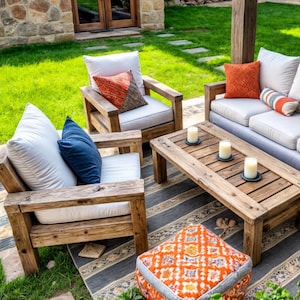 Könnte beinhalten: Ein Gartenmöbelset aus Holz mit einem weißen Sofa, zwei Stühlen, einem Couchtisch und einem gemusterten Hocker. Die Möbel sind auf einem gestreiften Teppich in einem Garten angeordnet.