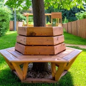 May include: A hexagonal wooden bench with a tree growing through the centre. The bench is made of natural wood and has a rustic look. The bench is surrounded by green grass.