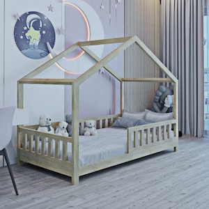 May include: A light wood children's bed with a house-shaped frame. The bed has a white mattress and a white and grey patterned pillow. There are three teddy bears on the bed. The wall behind the bed is pink with a white crescent moon and stars. The ceiling has a blue and white starry pattern.