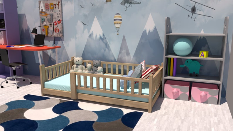 May include: A light wood toddler bed with a blue and white patterned rug, a grey bookshelf with two pink storage bins, and a blue and white hot air balloon on a wall with a mountain scene.