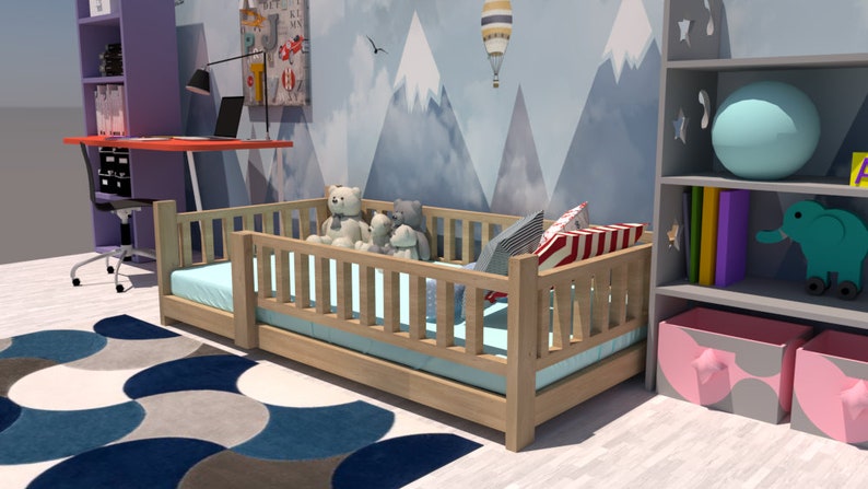 May include: A wooden toddler bed with a blue and white patterned mattress and a white, blue, and red striped pillow. The bed is surrounded by a wooden railing and has a few stuffed animals sitting on it. The bed is in a room with a blue and grey mountain-themed wallpaper.