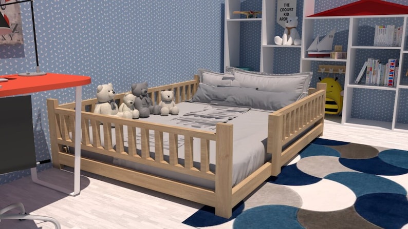 May include: A wooden toddler bed with a grey mattress and white pillows. The bed has a safety rail on all sides and is decorated with stuffed animals. The bed is in a room with a blue patterned wall and a white bookshelf.