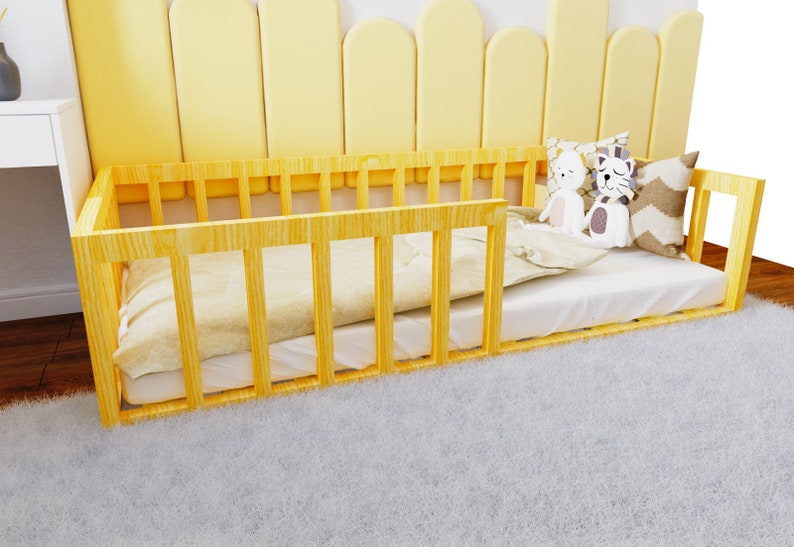 May include: A yellow wooden toddler bed with a white mattress and a white and brown patterned pillow. The bed is on a white fluffy rug.