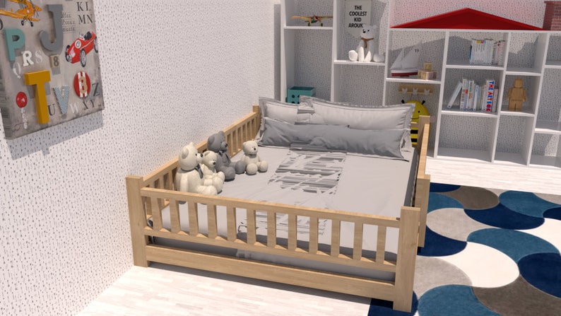 May include: A wooden toddler bed with a grey and white patterned bedding set. Four plush teddy bears are sitting on the bed. The bed has a wooden railing around the perimeter. The bed is in a room with a white wall and a white bookshelf with books and toys.