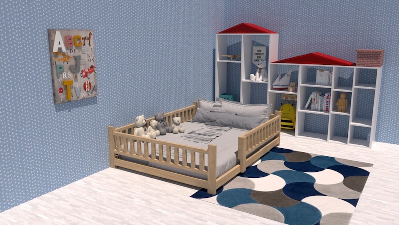 May include: A wooden toddler bed with a white and gray patterned sheet and a white pillow. There are four stuffed animals on the bed. The bed has a wooden railing around it. There is a blue and white rug on the floor. There are two white shelves with red roofs in the background. The shelves are filled with books and toys. The wall is light blue with a white pattern.