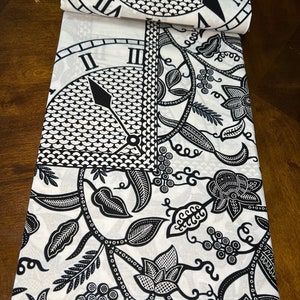 May include: Black and white fabric with a repeating pattern of a clock face and floral designs. The fabric has a green label with the text "Reee H 991992 3333 2000000 00000000 010101 VII VII M" on it.