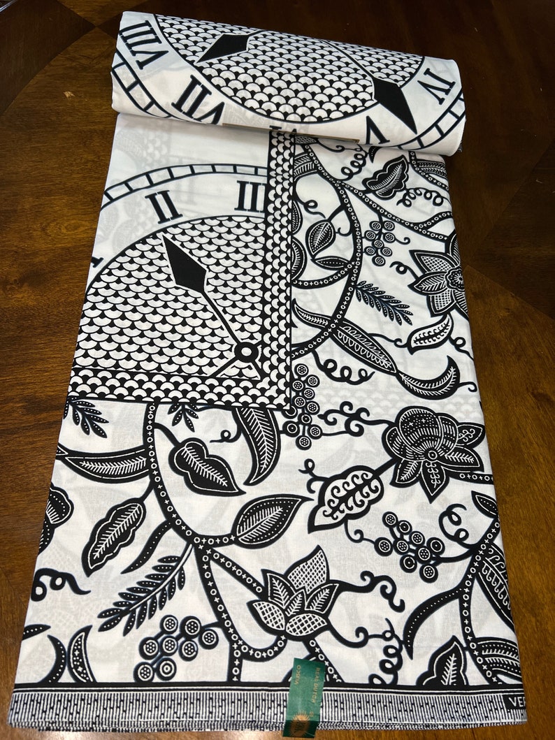 May include: Black and white fabric with a repeating pattern of a clock face and floral designs. The fabric has a green label with the text "Reee H 991992 3333 2000000 00000000 010101 VII VII M" on it.