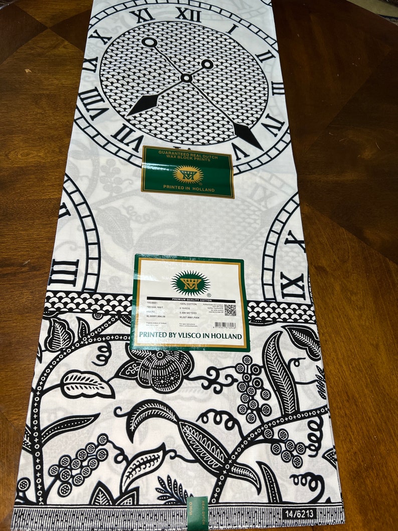 May include: Black and white fabric with a clock and floral pattern. The fabric has a label that says "Guaranteed Real Dutch Wax Block Print" and "Printed in Holland".