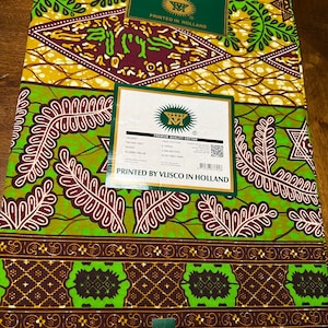 Peut inclure: Un tissu vert, marron et jaune avec un motif g&eacute;om&eacute;trique. Le tissu est &eacute;tiquet&eacute; "Guaranteed Real Dutch Wax Block Prints" et "Printed by Vlisco in Holland".