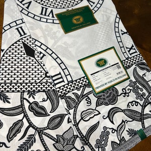 May include: Two white fabric panels with a black and white clock face design and a floral pattern. The fabric is labeled "Guaranteed Real Dutch Wax Block Prints" and "Printed by Visco in Holland".
