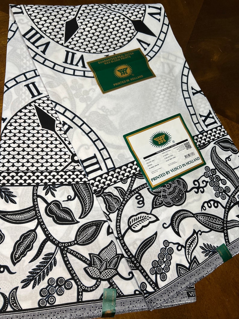 May include: Two white fabric panels with a black and white clock face design and a floral pattern. The fabric is labeled "Guaranteed Real Dutch Wax Block Prints" and "Printed by Visco in Holland".