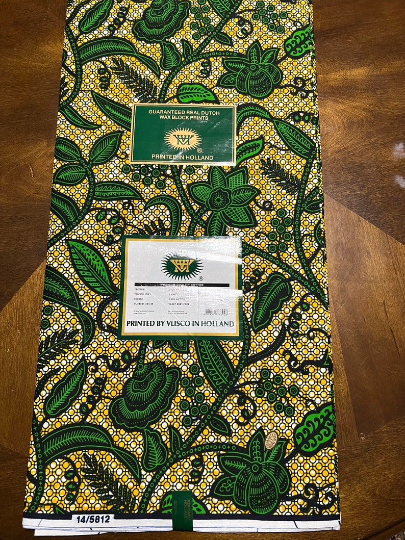 K&ouml;nnte beinhalten: Ein gelber und gr&uuml;ner Stoff mit einem Blumenmuster. Der Stoff ist bedruckt mit dem Text "Guaranteed Real Dutch Wax Block Prints" und "Printed in Holland".