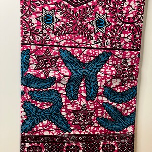 Op de afbeelding: Een levendige stof met een herhalend patroon van roze, zwarte en blauwe ontwerpen. De stof heeft Davidster-vormen, bladachtige motieven en geometrische randen. Het algehele ontwerp is een mix van gedurfde kleuren en ingewikkelde details.