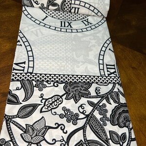 May include: Black and white fabric with a repeating pattern of a clock face and floral designs. The fabric has a green label with the text "14/6213".