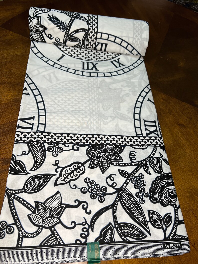 May include: Black and white fabric with a repeating pattern of a clock face and floral designs. The fabric has a green label with the text "14/6213".