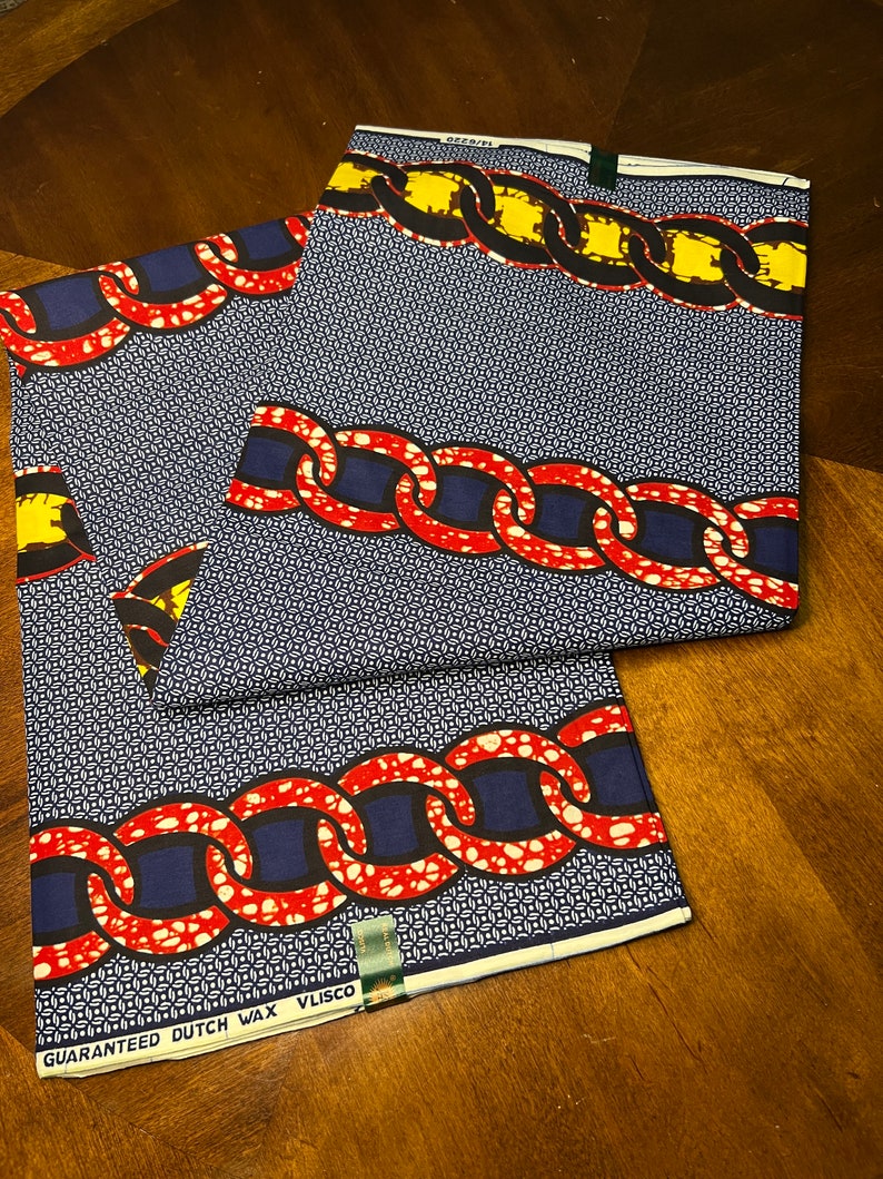 K&ouml;nnte beinhalten: Zwei St&uuml;cke Stoff mit Muster, mit blauem Hintergrund und einem Kettendesign in Rot, Gelb und Schwarz. Der Stoff hat ein geometrisches Muster und den Text "GUARANTEED DUTCH WAX VLISCO".