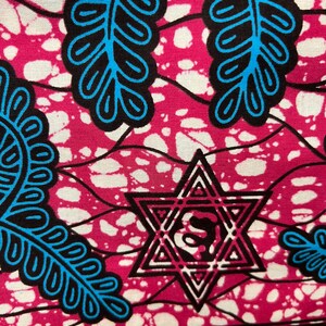 Op de afbeelding: Close-up van een levendige stof met een herhalend patroon. Het ontwerp heeft een magenta achtergrond met witte spikkels, zwart-blauwe bladachtige vormen en een Davidster. Een decoratieve rand loopt langs de onderkant.