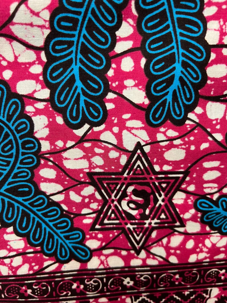 Op de afbeelding: Close-up van een levendige stof met een herhalend patroon. Het ontwerp heeft een magenta achtergrond met witte spikkels, zwart-blauwe bladachtige vormen en een Davidster. Een decoratieve rand loopt langs de onderkant.