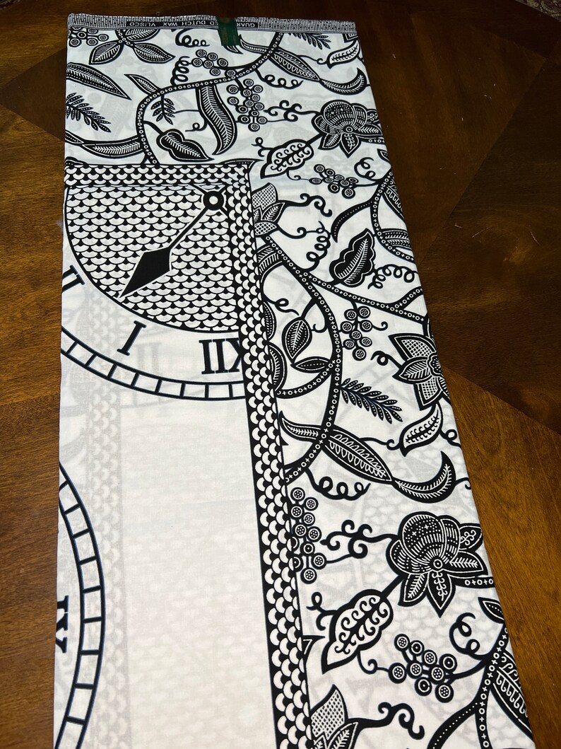 May include: Black and white fabric with a clock face and floral pattern. The fabric is folded in half.