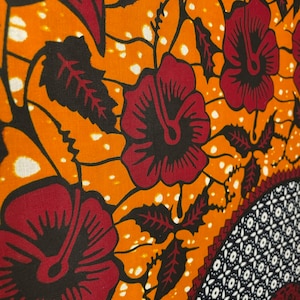 May include: Orange fabric with a repeating pattern of red flowers, black leaves, and white dots.