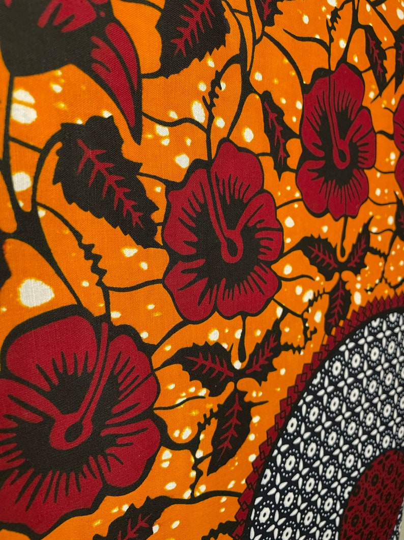 May include: Orange fabric with a repeating pattern of red flowers, black leaves, and white dots.
