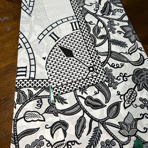 May include: Black and white fabric with a repeating pattern of a clock face and floral vines. The clock face has Roman numerals and a black hand.