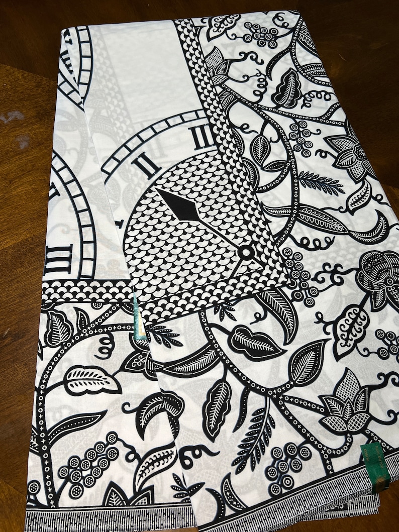 May include: Black and white fabric with a repeating pattern of a clock face and floral vines. The clock face has Roman numerals and a black hand.