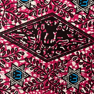 Op de afbeelding: Een levendig textiel met een herhalend patroon van witte stervormen met een blauwe letter 3, zwarte ruitvormen en bladmotieven op een magenta achtergrond. De stof heeft een getextureerd uiterlijk.