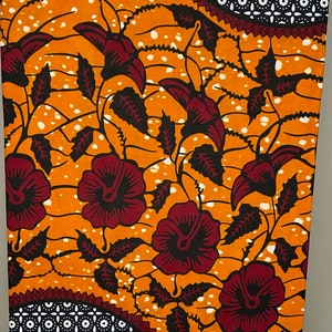 May include: Orange and white fabric with a repeating pattern of red flowers and black leaves. The fabric has a geometric pattern in the corners.