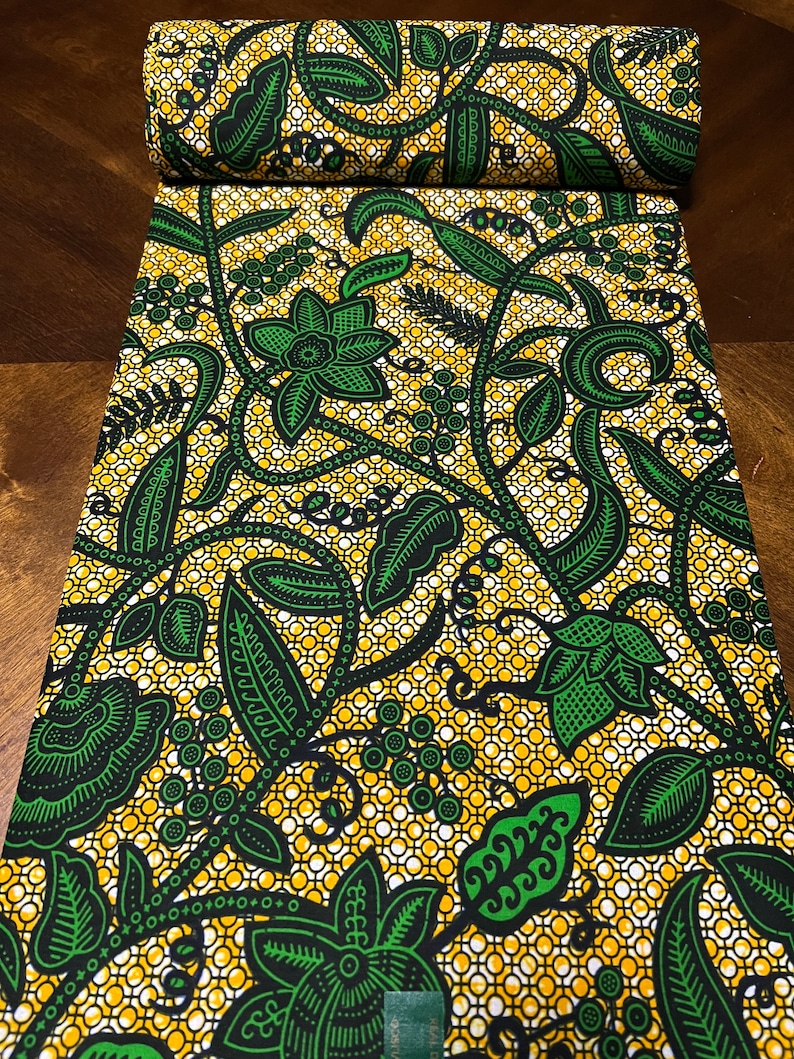 K&ouml;nnte beinhalten: Ein gelber und gr&uuml;ner Stoff mit einem Blumenmuster. Der Stoff hat ein sich wiederholendes Muster aus gr&uuml;nen Bl&auml;ttern und Blumen auf gelbem Hintergrund mit einem wei&szlig;en und schwarzen Gitter.