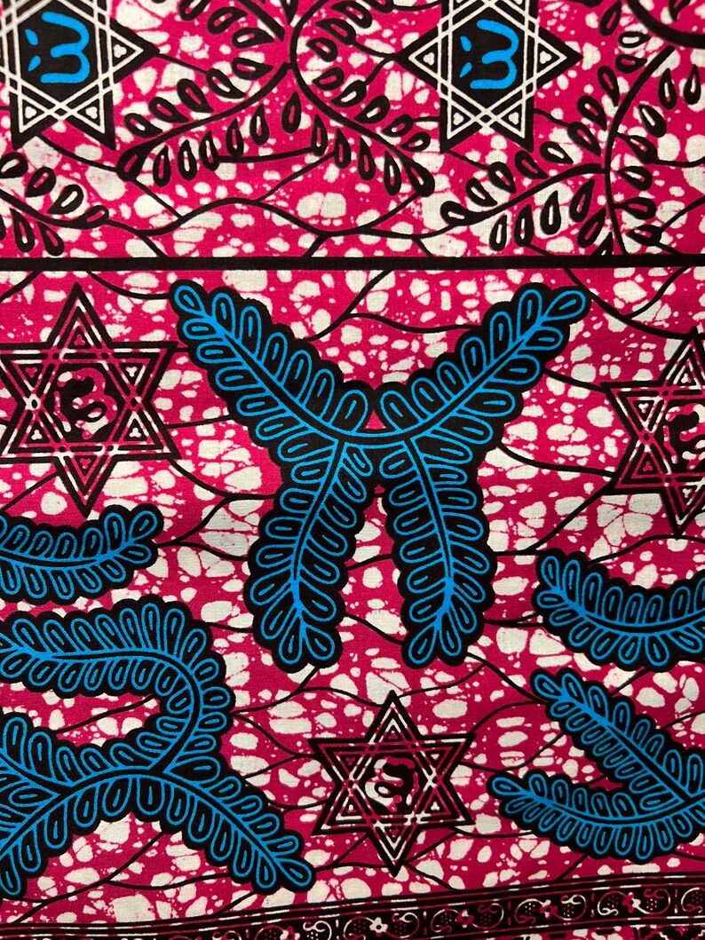 Op de afbeelding: Close-up van een levendige stof met een herhalend patroon. Het ontwerp heeft een magenta achtergrond met witte spikkels en zwarte en blauwe geometrische vormen, waaronder sterren en bladachtige motieven. De stof heeft een getextureerde uitstraling.