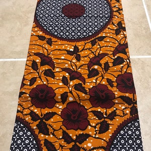 May include: A brown and white patterned fabric with a floral design. The fabric has a repeating pattern of circles with a smaller circle in the center. The fabric is made in Ghana.